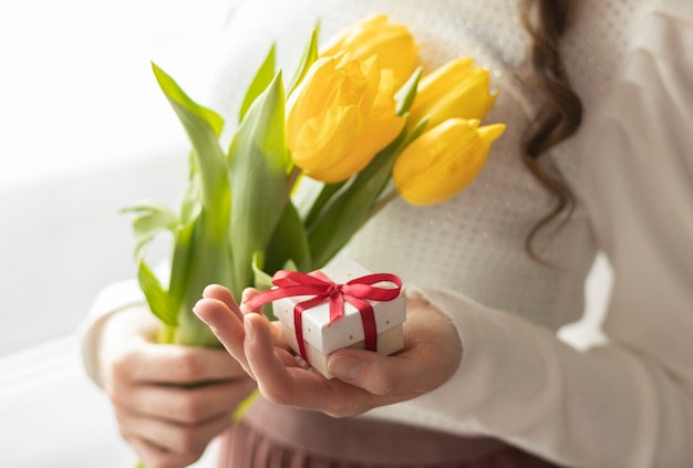 Manos femeninas sostienen tulipanes y caja de regalo en escritura