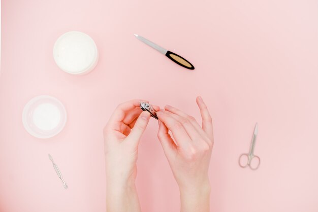 Manos femeninas con tarro de crema blanco, kit de manicura, tijeras, pulidor.