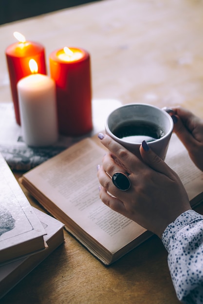 Manos femeninas con una taza de café cerca de libros y velas