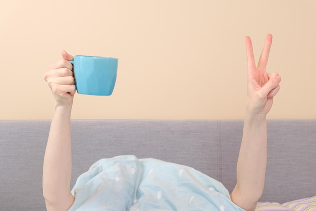 Manos femeninas con una taza de café y muestran un signo de gesto de victoria