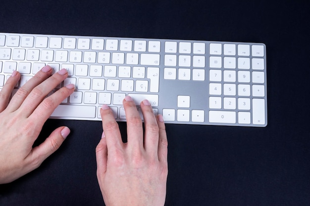 Manos femeninas en el teclado blanco y plateado sobre negro