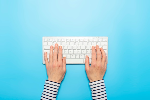 Manos femeninas en un teclado sobre un fondo azul. Concepto de trabajo de oficina, independiente, en línea.