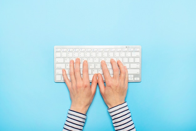 Manos femeninas en un teclado sobre una superficie azul. Concepto de trabajo de oficina, independiente, en línea. . Vista plana, vista superior