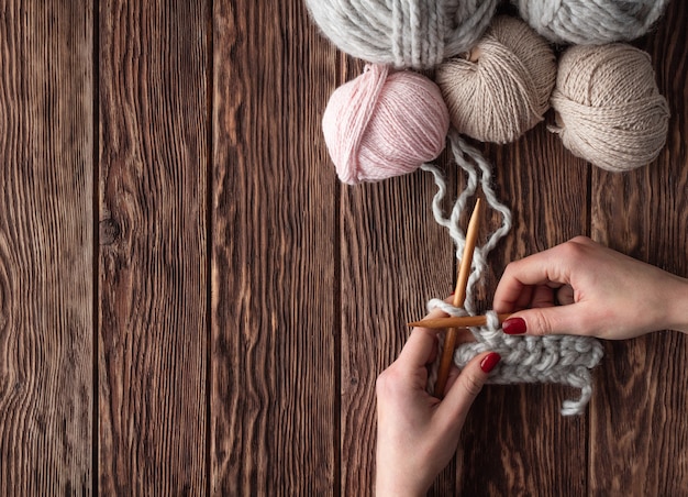 Manos femeninas tejer en una mesa de madera con bolas de hilo. Concepto hecho a mano.