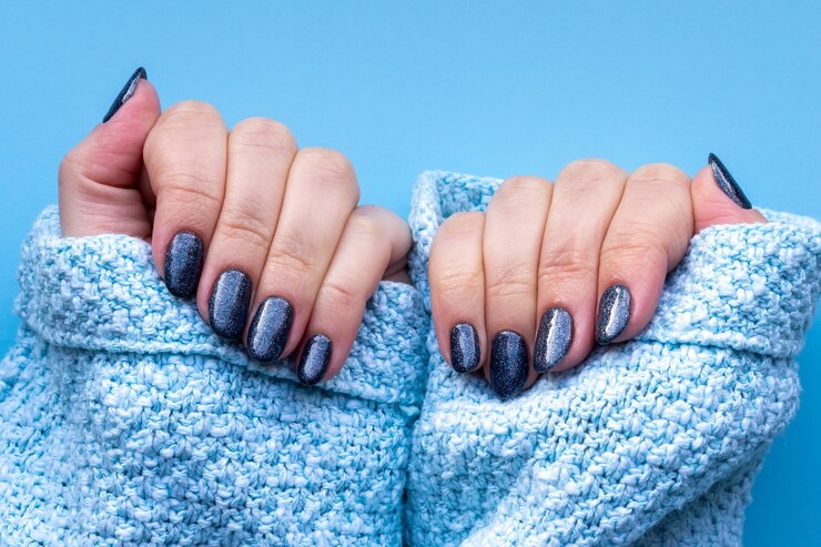 Manos femeninas en tejido de suéter de punto con hermosa manicura - uñas brillantes de color azul oscuro sobre fondo azul. Enfoque selectivo. Vista de cerca
