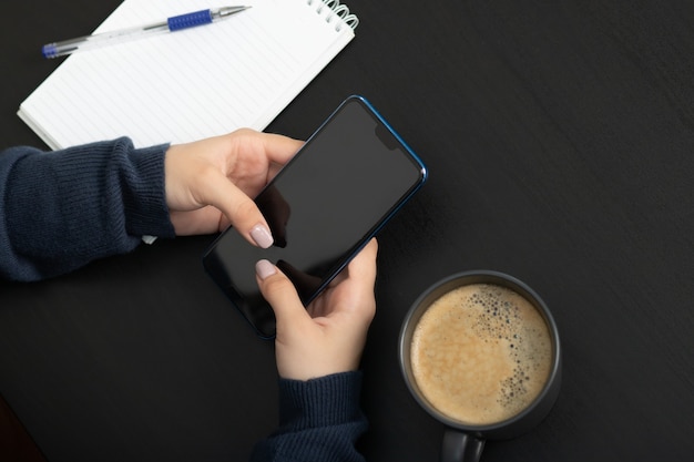 Manos femeninas con un teléfono inteligente en una mesa escribiendo texto en la pantalla