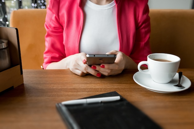 Manos femeninas con un teléfono negro, una taza de café