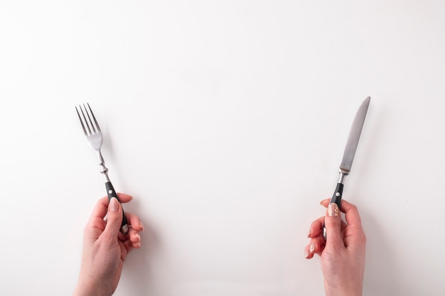 Manos femeninas con tenedor y cuchillo en blanco