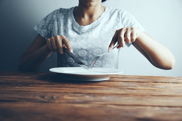 Manos femeninas con tenedor y cuchillo sobre el plato vacío