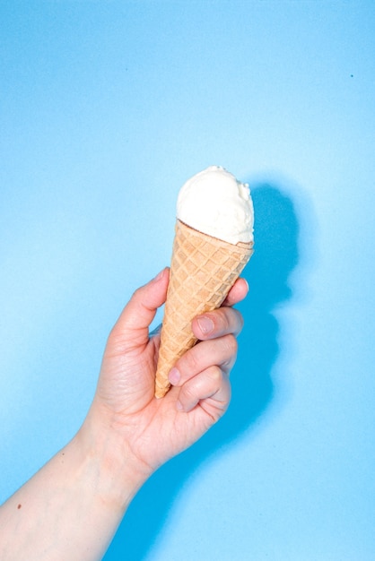 Manos femeninas tiene varios helados sobre fondo azul.