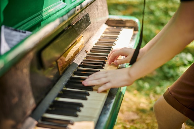 Manos femeninas tocando un piano antiguo en un parque público al aire libre, espectáculo de música artística, vista de cerca