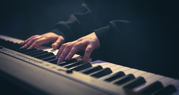 Manos femeninas tocar las teclas del piano en una habitación oscura y brumosa