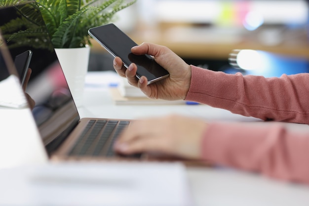 Las manos femeninas trabajan en una computadora portátil y mantienen aplicaciones de teléfonos inteligentes para computadoras y teléfonos inteligentes