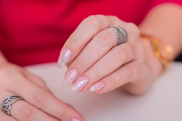 Manos femeninas con uñas de manicura de boda, esmalte de gel desnudo, sobre fondo rosa