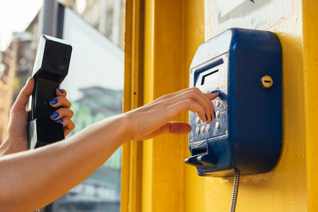 Manos femeninas usando el teléfono público en la ciudad.