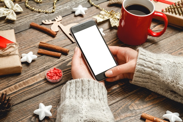 Manos femeninas utiliza el teléfono sentado en una mesa con accesorios navideños