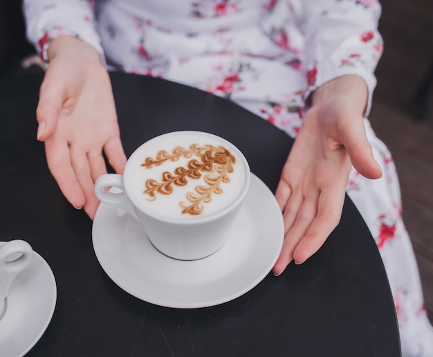 Manos femeninas en vestido sosteniendo una taza de café.