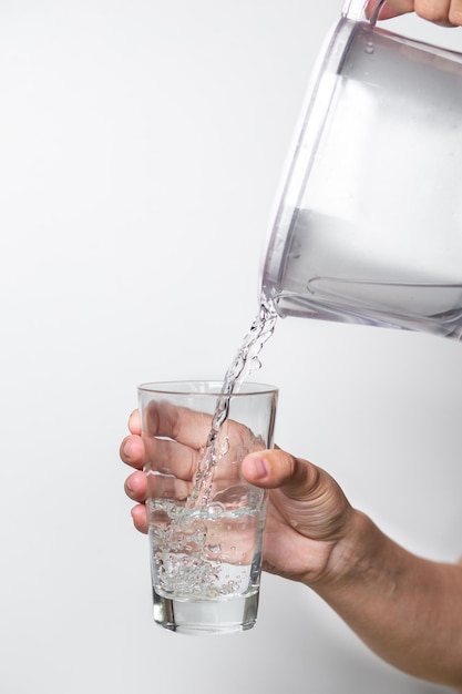 Las manos femeninas vierten agua limpia de una jarra de filtro en un vaso de precipitados sobre un fondo blanco.