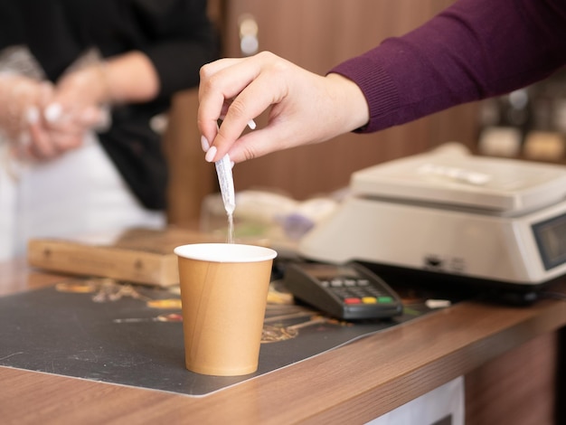 Las manos femeninas vierten azúcar del paquete en un vaso desechable