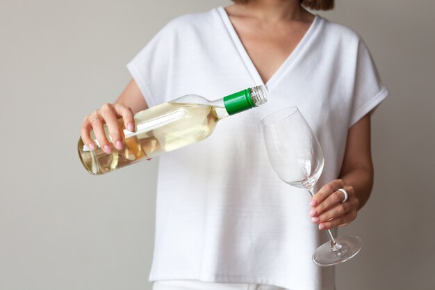 Manos femeninas vierten vino blanco de botella a copa