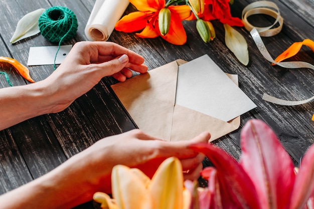 Manos del florista o del diseñador de la mujer joven que crea la tarjeta de felicitación en la tabla de madera con las flores coloreadas