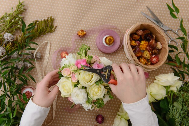 Manos de floristería haciendo ramo de flores de rosas. Ver en la mesa desde arriba.