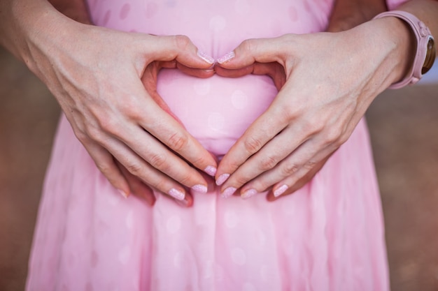 Manos en forma de corazón de la mujer embarazada y su marido