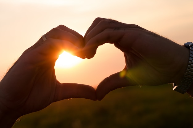 manos formando una forma de corazón al atardecer