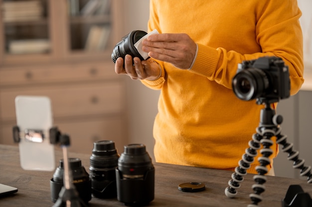 Foto manos de fotógrafo de stock profesional arreglando la cámara fotográfica en un trípode frente al teléfono inteligente mientras da lecciones para la audiencia en línea