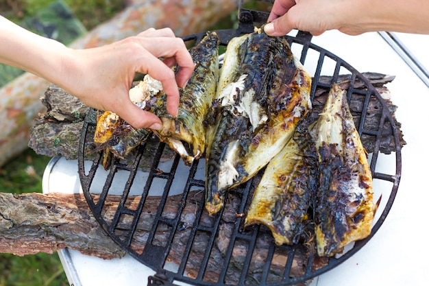 Las manos de la gente llevan el pescado a la parrilla.