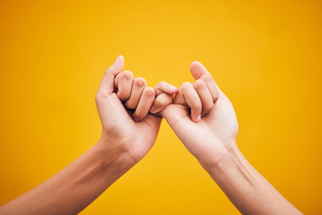 Las manos de la gente y el meñique prometen en el estudio con ayuda de confianza o esperanza de reconciliación sobre fondo amarillo Emoji de dedo y trato de amigos con gesto secreto y expresión de apoyo o solidaridad