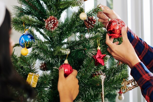 Manos de gente de negocios decorando el árbol de Navidad en la oficina con adornos de colores