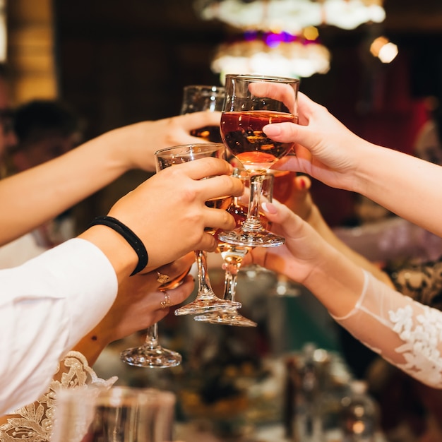 Manos de un grupo de personas tintineando y tostando copas de vino tinto en una fiesta festiva en un restaurante