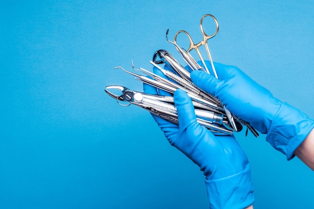 Manos en guantes azules sosteniendo equipos dentales e instrumentos de metal sobre fondo azul.