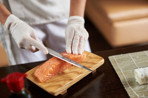 Manos en guantes desechables rebanar salmón sobre plancha de madera