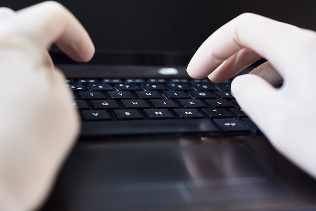 Manos en guantes escribiendo en el teclado del ordenador portátil. Concepto de protección contra virus