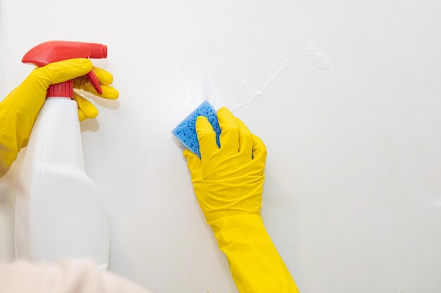 Manos con guantes de goma amarillos lavando los azulejos en el baño.