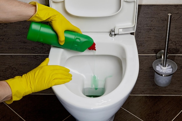 Las manos con guantes de goma amarillos vierten desinfectante en el inodoro