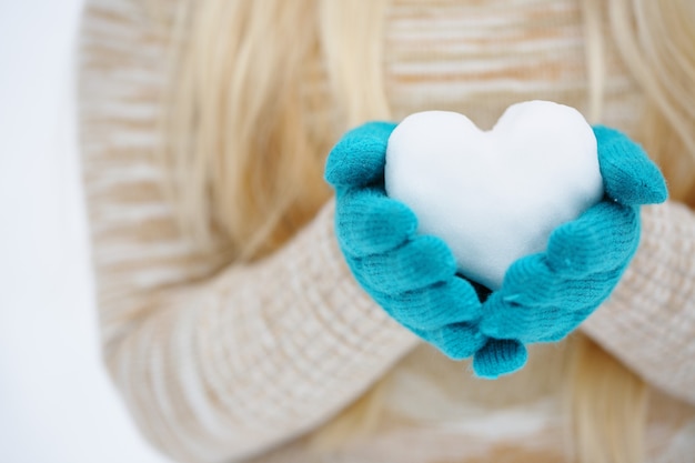 Las manos en guantes mantienen el corazón fuera de la nieve