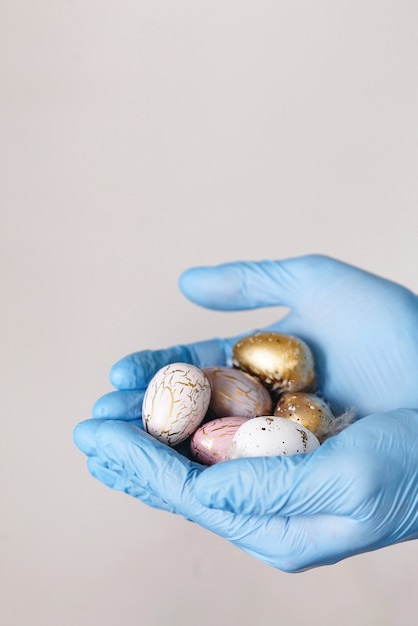 Manos en guantes médicos con huevos de Pascua pintados modernos. Enfoque selectivo. Imagen tonificada. Aislado.