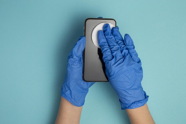 Foto las manos con guantes médicos limpian la pantalla del teléfono inteligente con un paño desinfectante el primer plano de las manos está limpiando el teléfono móvil aislado sobre fondo azul desinfección de teléfonos inteligentes