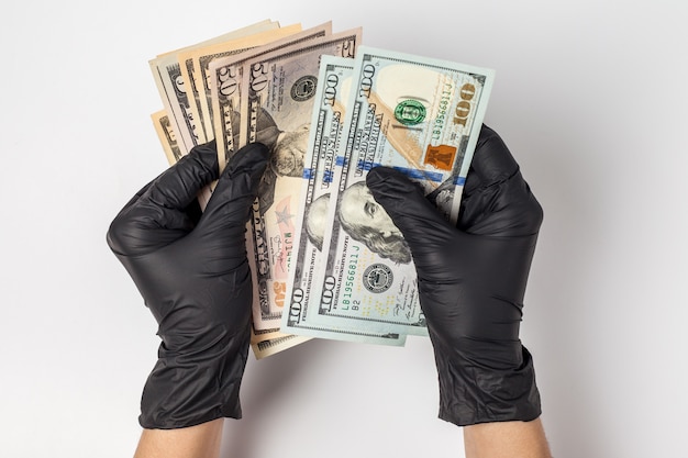 Manos en guantes médicos sosteniendo un paquete de dólares. El concepto de infección por dinero, dinero sucio.