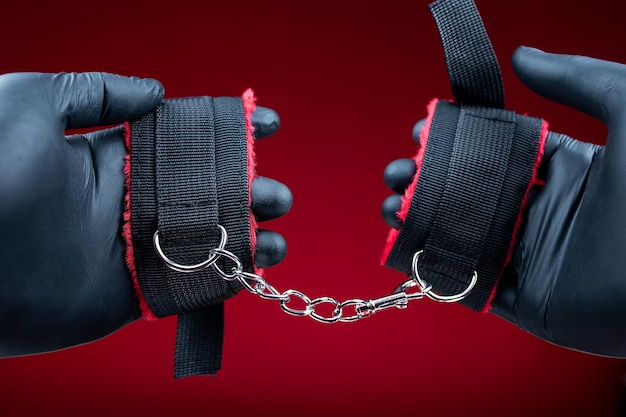 Foto manos en guantes negros con esposas con cinturones rojos para juegos sexuales bdsm