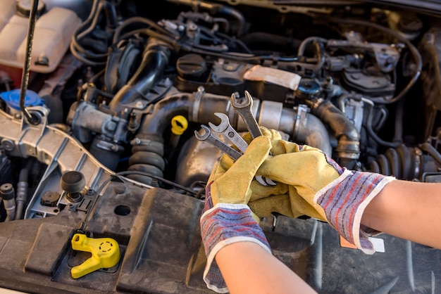 Manos en guantes protectores con llaves contra el motor del coche