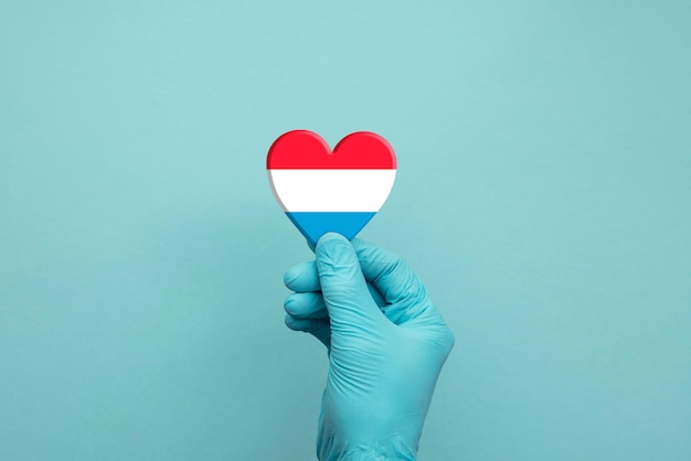 Manos con guantes quirúrgicos protectores con corazón de bandera de luxemburgo