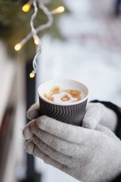 Las manos en guantes sostienen una taza de café caliente. Café para llevar en invierno.