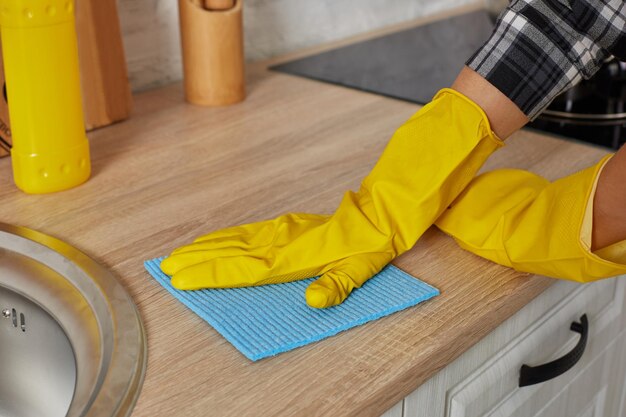 Manos en guantes con trapo verde está limpiando gabinetes de cocina - concepto de tareas domésticas y limpieza. De cerca