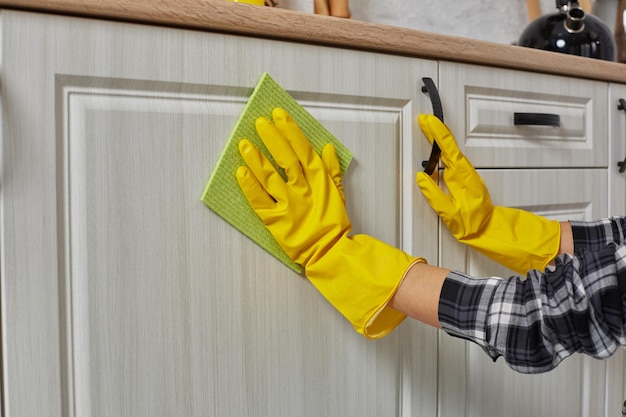 Las manos en guantes con un trapo verde están limpiando gabinetes de cocina, tareas domésticas y concepto de limpieza