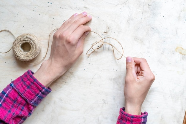 Las manos hacen un nudo de una cuerda gruesa con una bola de cuerda