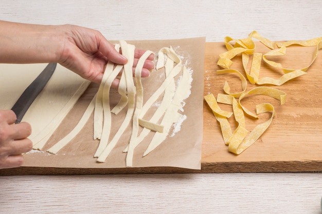 Las manos hacen pasta fresca hecha a mano. Masa enrollada, cortada en tiras